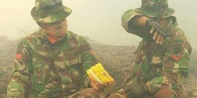 2 Anggota TNI berbagi mie instan di tengah kepulan asap